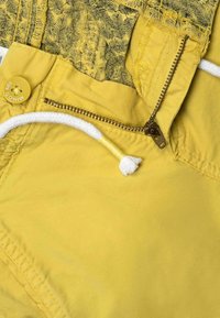 Gula shorts med ett texturerat blommönster vid midjan, dragkedja fram och en vit dragsko med gula detaljer.