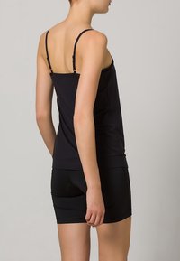 Sort tætsiddende tanktop med tynde justerbare stropper, glat tekstur og runding i kanten, sat sammen med en sort mininederdel.
