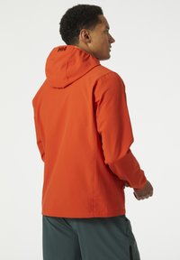 Chaqueta con capucha naranja de acabado texturizado, que presenta un logo en la parte posterior y mangas hasta la muñeca, combinada con pantalones cortos verde oscuro.