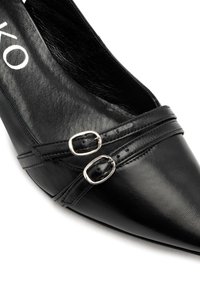 Pantofii din piele neagră cu vârf ascuțit, dotati cu două catarame argintii și accente cusute pe partea superioară. Textură netedă cu un finisaj lucios.