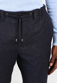 Marinblå texturerade byxor med dragsko i midjan, med ett prickigt mönster och metallaccessoarer, delvis täckta av en ljusblå tröja.