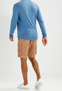 Lange mouwen blauwe shirt met een relaxte pasvorm, gecombineerd met beige cargoshorts met zijzakken, afgewerkt met witte sneakers.