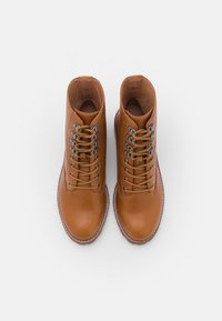 Brązowe skórzane botki za kostkę z metalowymi oczkami, płaskimi sznurowadłami, okrągłym noskiem i kontrastowym przeszyciem wokół podeszwy.