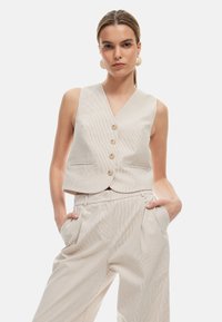 Beige gestreifter Weste mit V-Ausschnitt, fünf Knöpfen und zwei Seitentaschen, kombiniert mit passenden hoch taillierten Hosen. Sanfte Stofftextur.