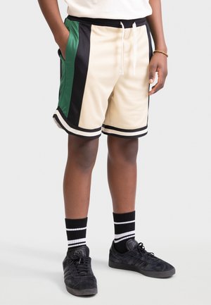 Crème shorts met zwarte, groene en witte accenten, voorzien van een trekkoord in de taille en zijzakken. Draag ze met zwarte schoenen en gestreepte sokken.