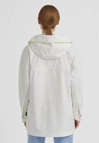 Weiße wasserdichte Jacke mit Kapuze, im lässigen Schnitt, großen Ärmeln und verstellbaren Handgelenkbündchen. Glatte, glänzende Textur.