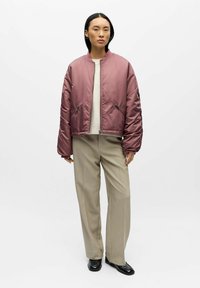 Polstret bomberjakke i lavendel med en glatt satengfinish, med to glidelåslommer på sidene og en ribbestrikket krage, båret over en kremfarget genser og beige bukser.