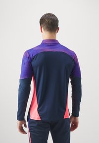 Langärmliges Sporthemd in Marineblau mit lila und pinken Akzenten, das ein strukturiertes Oberdesign und einen Stehkragen aufweist.