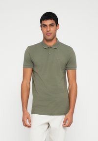 Oliwkowa koszulka polo z krótkim rękawem, kołnierzykiem i subtelnym logo. Wykonana z miękkiego bawełnianego materiału, charakteryzuje się dopasowanym krojem i czystymi liniami.