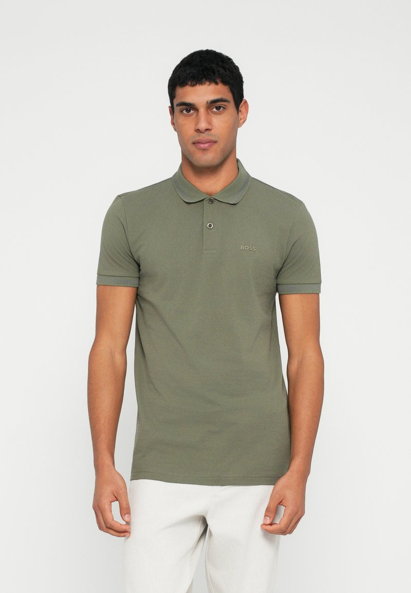 Oliwkowa koszulka polo z krótkim rękawem, kołnierzykiem i subtelnym logo. Wykonana z miękkiego bawełnianego materiału, charakteryzuje się dopasowanym krojem i czystymi liniami.