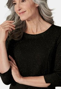 Schwarzes Kleid mit goldenen Sprenkeln, rundem Ausschnitt, 3/4-Ärmeln und glatter Textur. Nahaufnahme zeigt Hände und einen sanft strukturierten Ausschnitt.