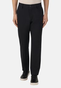 Černé kalhoty se rovnou nohavicí vyrobené z hladkého materiálu. Mají páskové smyčky a knoflíkové zapínání vpředu, doplněné o černé tenisky.