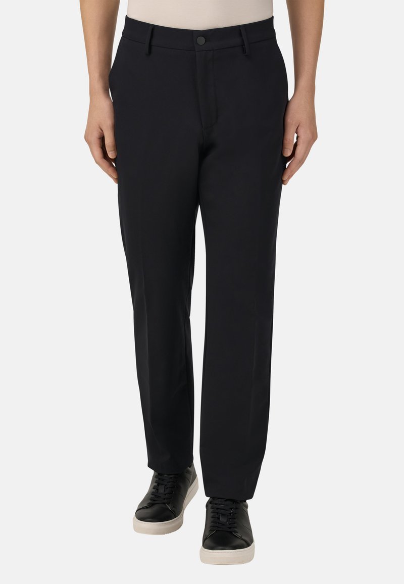 Černé kalhoty se rovnou nohavicí vyrobené z hladkého materiálu. Mají páskové smyčky a knoflíkové zapínání vpředu, doplněné o černé tenisky.