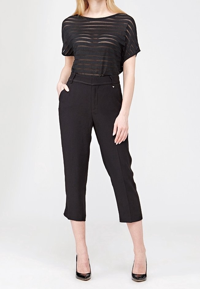 Černý průhledný pruhovaný top s širokými rukávy v kombinaci s černými kalhotami s vysokým pasem a zkrácenou délkou. Modelka má na sobě černé vysoké podpatky, na jednobarevném pozadí.
