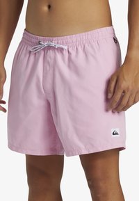 Bañador corto rosa hecho de una tela ligera, con cinturilla elástica, cordón ajustable, bolsillos laterales y detalle de parche con logo.
