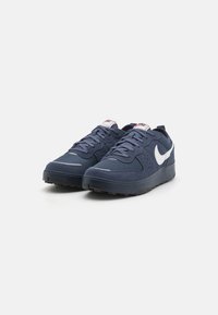 Navy blue sneakers with a suede and mesh upper, featuring a white logo, grey accents, and a textured rubber sole for traction.