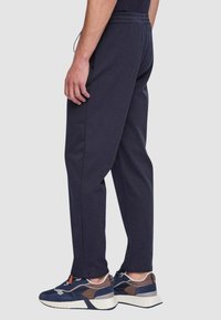 Pantaloni della tuta blu navy con vestibilità rilassata, vita elastica, tasche laterali, abbinati a sneakers blu navy con accenti grigi e suole bianche.