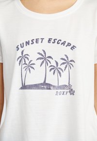 Biele tričko s potlačou textu "SUNSET ESCAPE" a grafikou paliem na malom ostrove. Dizajn je natlačený tmavo fialovou farbou.