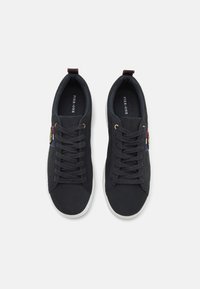 Baskets noires en toile avec un dessus texturé, semelle blanche et œillets dorés. Comprend une étiquette multicolore avec logo sur le côté.