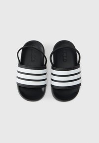 Μαύρες σαγιονάρες με υφή στο επάνω μέρος και αντίθετες λευκές ρίγες. Διαθέτουν λείες σόλες και ρυθμιζόμενο λουράκι για σταθερή εφαρμογή.