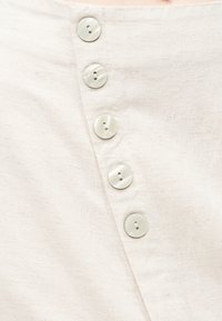 Διαγώνια σειρά από πέντε στρογγυλά, εκρού κουμπιά σε υφασμάτινη βάση μπεζ με υφή, πιθανώς μέρος ενός κουμπώματος ρούχου.