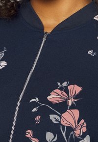 Giacca con zip a fiori navy con motivi di fiori rosa e grigi, con colletto a costine e zip metallica per la chiusura. Tessuto morbido.
