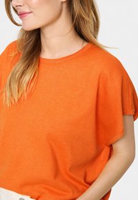 Oranssi lyhythihainen neulepaita, jossa on rento leikkuu. Ominaisuuksiin kuuluu pyöreä kaula-aukko ja pehmeä rakenne, joka korostaa sulavaa ja rentoa ilmettä.