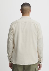 Helle beige Langarmbluse mit Button-Down-Kragen, einfacher Yoke und schwarzen Knopfakzenten an den Manschetten. Baumwollstruktur, lässige Passform.