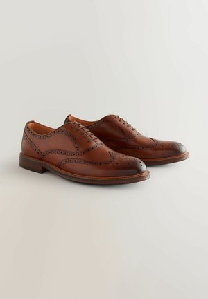 Chaussures brogue en cuir marron avec un bout rond, un design à lacets, des perforations délicates et un capuchon de bout sombre contrastant. Texture lisse.