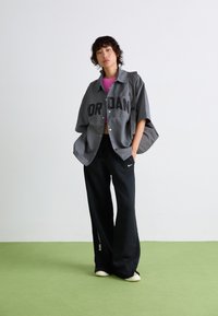 Oversized gray button-up shirt with "JORDAN" text, pink crop top underneath, black sweatpants with white logo, and cream shoes. Textured fabric.