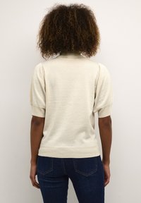 Pull en beige clair à manches courtes, avec un ourlet côtelé et une finition douce et texturée. Porté avec un jean en denim foncé.