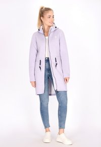 Šviesiai purpurinė ilga hoodie, pagaminta iš minkštos medžiagos, su užtrauktuku, reguliuojamomis raišteliais ir dviem šoninėmis kišenėmis. Suderinta su liesomis džinsinėmis kelnėmis.