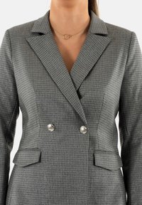 Blazer grigio a quadri con design doppiopetto, bottoni argentati, rever affilati e tasche laterali, realizzato in tessuto texturizzato.