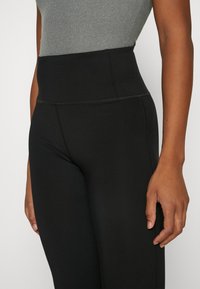 Czarne legginsy wysokiej talii wykonane z elastycznej tkaniny o gładkiej fakturze, z płaskimi szwami i bez widocznych kieszeni.