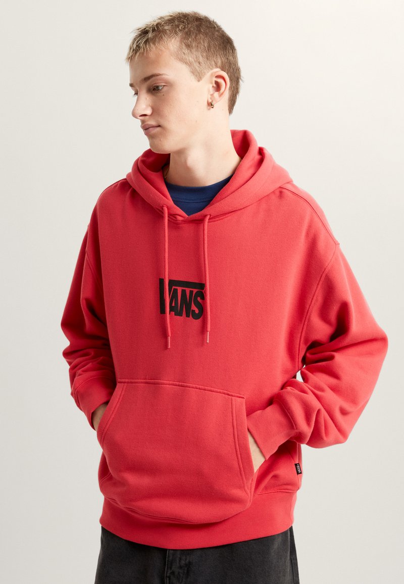 Sweat à capuche rouge en coton, doté d'une poche avant, d'une capuche avec cordon de serrage et d'un logo "VANS" noir au centre. Texture lisse, coupe classique.
