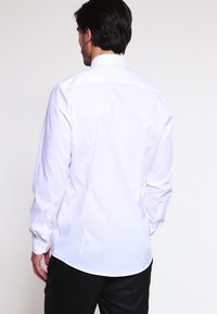 Weißes Langarmhemd mit klassischem Kragen, glatter Textur und abgerundetem Saum. Verfügt über Knopfmanschetten und eine taillierte Passform mit Rückennähten.