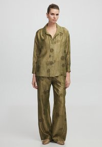 Ensemble coordonné en tissu léger de couleur vert olive, comprenant une chemise et un pantalon, avec un motif floral. La chemise a un col et une fermeture à boutons.