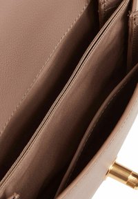 Interior de bolso de cuero marrón con dos compartimentos abiertos y un forro con textura. Herrajes dorados y detalles de costura prolijos visibles.