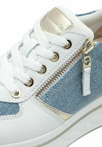 Sneaker da donna con tomaia in pelle bianca, dettagli in tessuto di denim, elementi in metallo dorato e una cerniera laterale. Presenta lacci bianchi e una suola testurizzata.