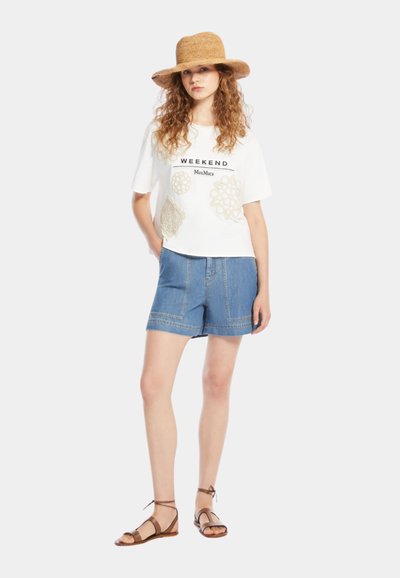 Tricou alb cu textul "WEEKEND MaxMara" și accente tip croșetat, asortat cu pantaloni scurți din denim albastru și sandale maro. O pălărie din paie completează look-ul.
