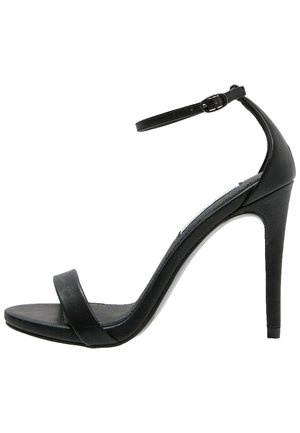 Sandale noire à talon haut avec fine bride à la cheville et boucle, bout ouvert, et une seule bride avant, vue de côté sur fond blanc.