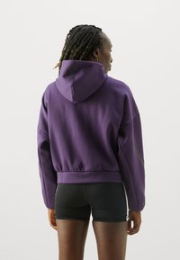 Lila kort hoodie med huva, långa ärmar och svarta accentdetaljer. Parat med svarta shorts som visar en avslappnad passform och mjuk textur.