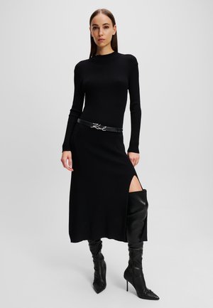 Juodas raukšlėtas megztinis su ilgomis rankovėmis, šonine skyle ir juodu diržu su sidabro "Karl" logotipu. Dėvėta su blizgiais juodais aukštakulniais. 