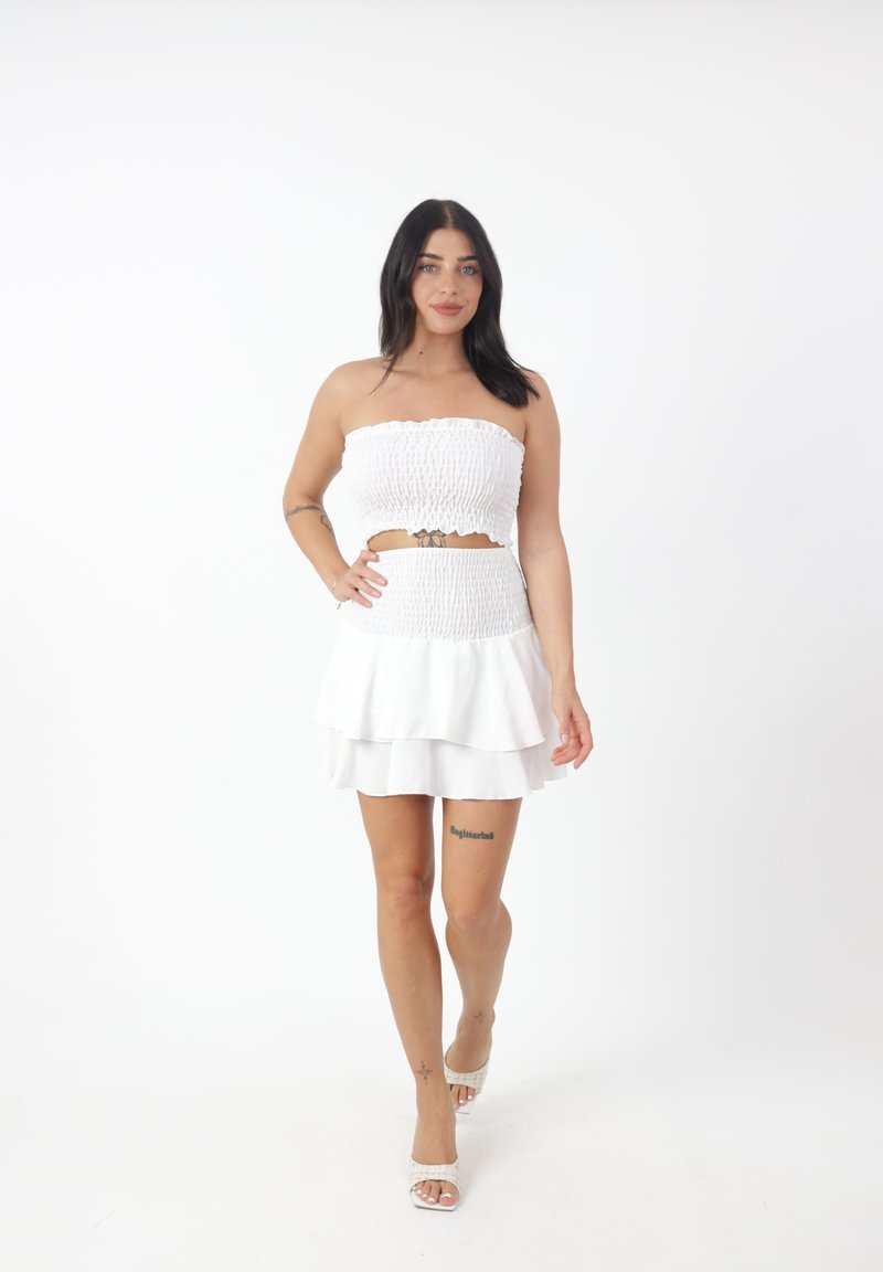 Conjunto blanco de dos piezas que incluye una blusa sin tirantes con fruncido y una falda con volantes. La tela tiene una textura suave y un diseño ajustado.