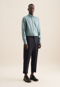 Chemise bleu clair à manches longues, assortie à un pantalon bleu marine foncé et des chaussures noires à lacets. Tissu lisse et design ajusté.