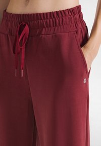 Bordeaux joggers met een ontspannen pasvorm, elastische tailleband, trekkoord, zijzakken en een klein logo-accent op de onderzoom.