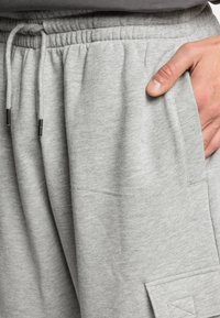 Grijze sweatpants met een trekkoord in de taille, zijzakken en een gestructureerde afwerking. Heeft een vierkante patch-detail op het rechterbeen.