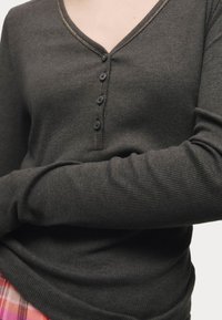 Top lungo a maniche lunghe grigio scuro a coste con scollatura a V, dotato di cinque bottoni neri e dettagli in cucitura marrone chiaro lungo il collo.