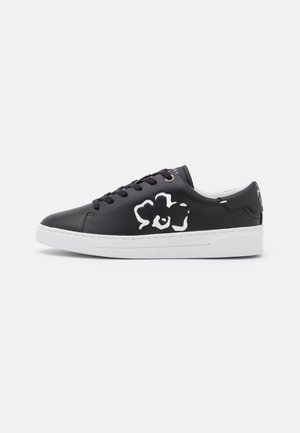 Sneaker en cuir noir avec un motif floral blanc sur le côté, semelle en caoutchouc blanche, bout rond et lacets noirs. Design minimaliste et moderne.