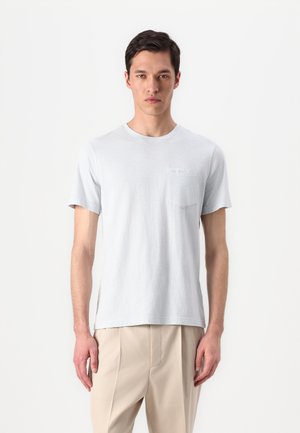 T-shirt à manches courtes gris clair en tissu doux et respirant, avec un col rond et une petite poche sur la poitrine. Présente une coupe décontractée et des fentes sur les côtés.